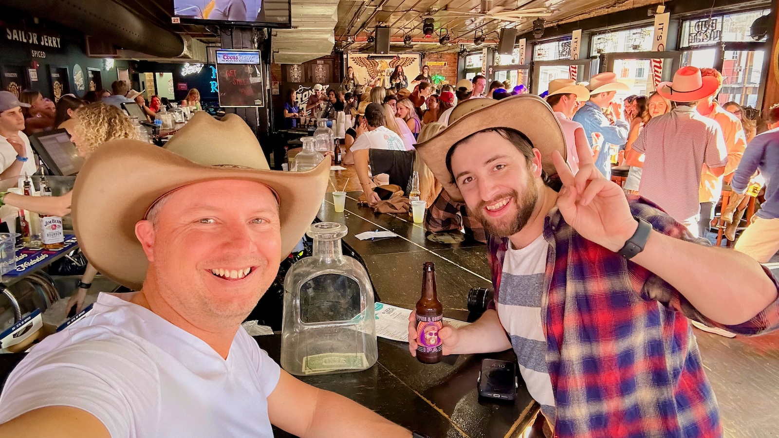 Two men in a bar wearing cowboy hats. Party behind them.