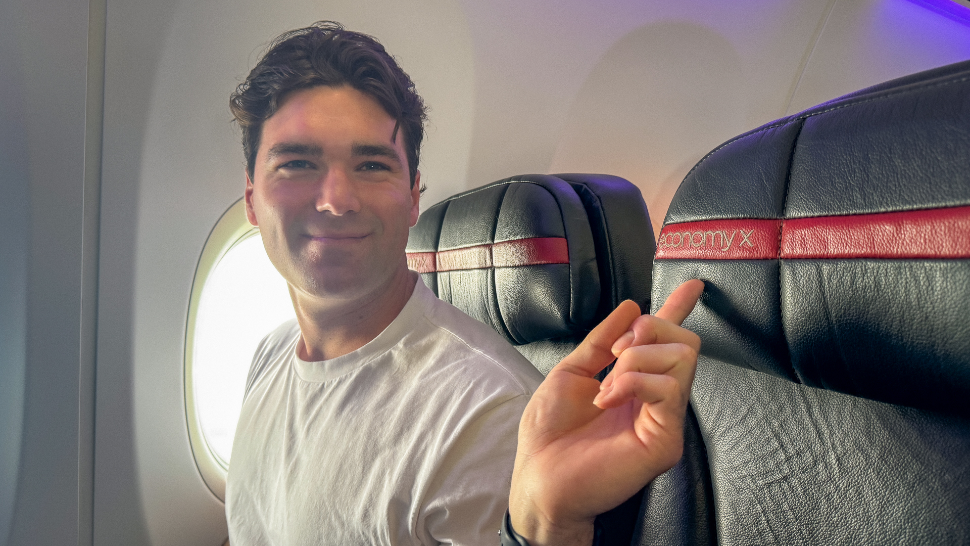 Josh Weckert pointing at the Economy X label on a Virgin Australia seat